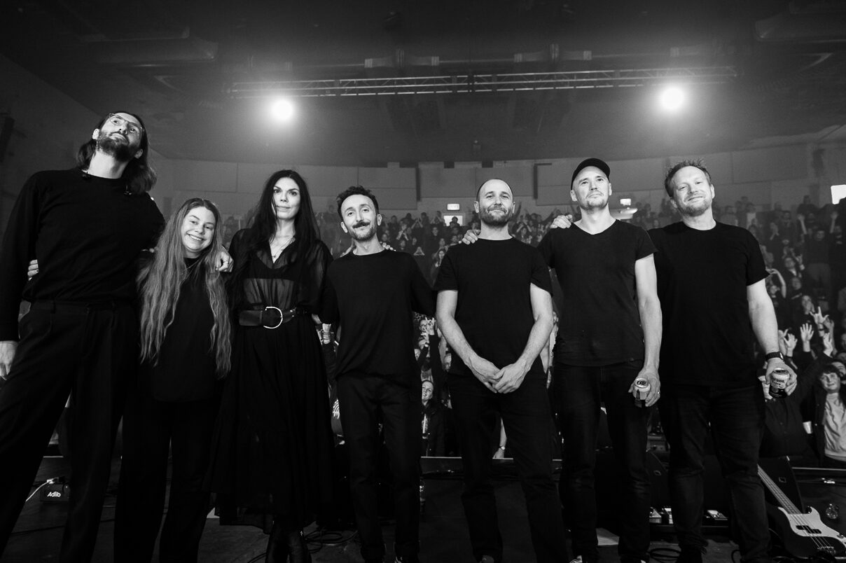 A photo of the members of the band Maybeshewill, plus string players Sophie Green and Alex Williams standing on with the audience behind them.